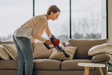 Young woman with rechargeable vacuum cleaner cleaning at home © Petro