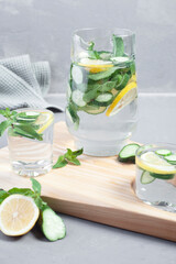 Delicious cold summer lemonade with cucumber and mint in stone jars on a light slate, stone or concrete background.