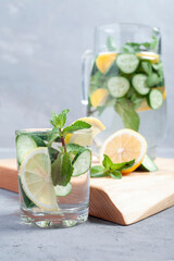 Water with cucumber, lime and mint on a gray rustic background. In a glass decanter