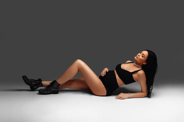 A beautiful pregnant girl in a black image lies on the white floor. Fashionable dark style. Beautiful pregnancy time