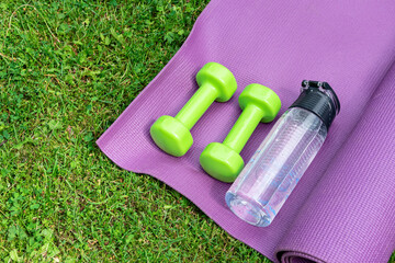 Ladie's dumbbles, fitness mat and sneakers on the green grass background