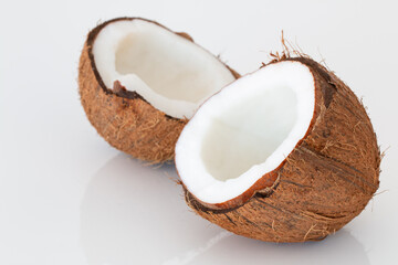 A coconut cut in half on a white, mirror background.