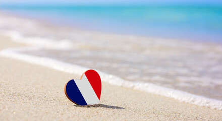 Flag of France in the shape of a heart on a sandy beach. The concept of the best vacation in French resorts