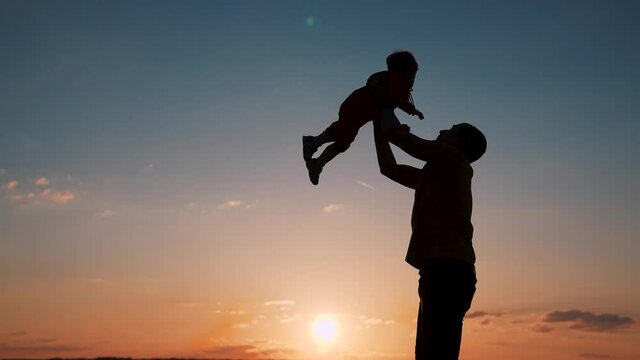 Silhouette of happy family. Father and son in park. Father tosses son up. Happy family concept. Father plays with son in park. Family silhouette. Father tosses his son up. Silhouette of happy family