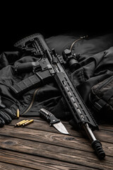 Modern automatic rifle with a telescopic sight on a dark background. Jacket, cap, gloves on a...