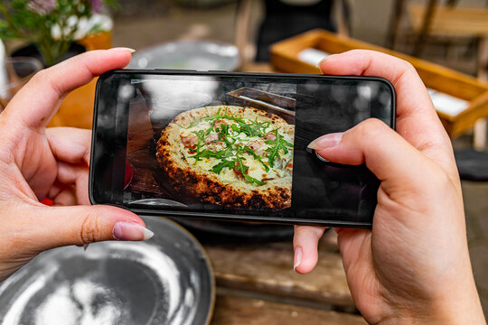 woman hand with smartphone photographing pizza at restaurant or cafe
