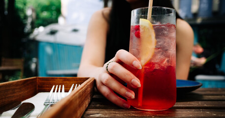 woman hand hold glass with lemonade cocktail at table in cafe outdoor