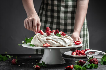 delicious homemade Pavlova cake with fresh strawberries and whipped cream. Female baker decorating delicious meringue cake