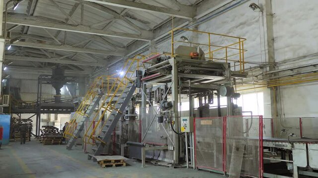 Bags of cement are moved along a roller conveyor on the territory of the plant. An industrial cement processing facility, the territory of the plant. Interior of the cement plant workshop