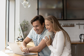 Happy affectionate loving young married family couple looking at computer screen, reading email with good news, planning vacation together, shopping in internet store or web surfing information.