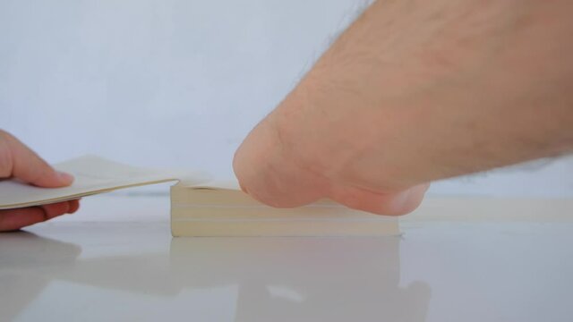 A man hand opens a book and it is on the white and shine polishing surface of table and fingers reflections on white ground