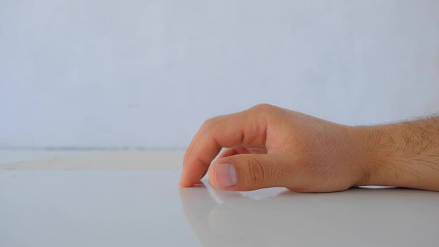 A man hand sign of waiting sign and putting his fingers on the white and shine polishing surface of table and fingers reflections on white ground.