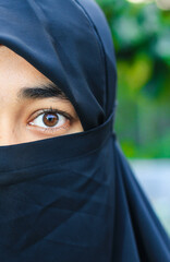 Closeup of beautiful woman face covered with hijab. Perfect shiny eyes of a Muslim girl. Young niqab girl portrait with the background.