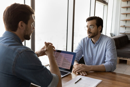 Skilled young male hr manager employer leader boss holding job interview with candidate, discussing previous working experience. Professional financial advisor consulting client at office meeting.