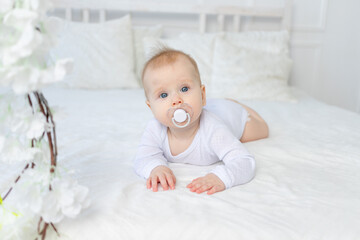 baby with a pacifier for six months on a white bed in the bedroom