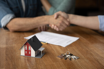 Close up focus on small house model and keys on table near paper contract agreement with client...