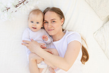 portrait of a mother with a baby in her arms gently embracing him on a white bed at home, mother's love