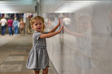 A little girl walks along the underground passage of the subway. A child near a gray wall. Children's safety in a public place. Game in the city.
