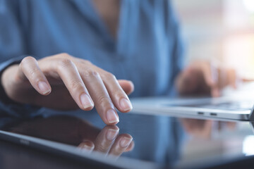 Close up of woman hand using digital tablet, finger touching on screen and working on laptop computer on table at home office