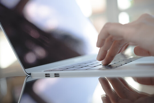 Closeup image of woman's hands working and typing on laptop keyboard on glass table with reflection