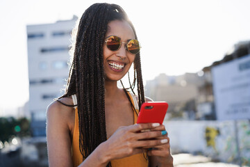 Bohemian mixed race girl using smartphone outdoor with city in background - Technology and trendy...