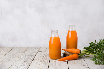 Carrot juice in glass bottles and carrots on a light wooden background with copy space. Gray background. Vegetarianism concept