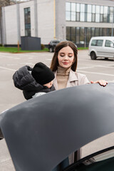 young woman with toddler son closing car trunk outdoors