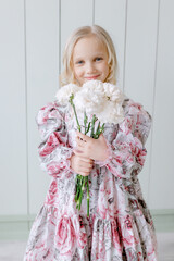 Little girl holding white carnations in her hands Stylish dress on her body European appearance with blue eyes blonde Posing for the camera childhood model