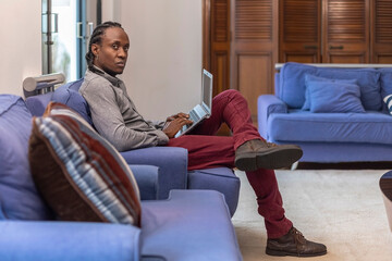 African descendant working on the couch with her laptop, looking at camera with serious expression.
