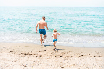 Naklejka premium Father and son running towards the ocean together during summer vacation