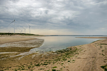 Fototapeta na wymiar Wide sandy beach with shallow puddles and wind turbines under a dramatic cloudy sky on Maasvlakte peninsula naer Rotterdam, The Netherlands