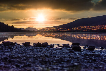 Sunset at Rotevatnet in Volda, Norway with citylights in background and stones in forefront