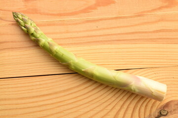 One stalk of green organic asparagus on a wooden table, close-up, top view.