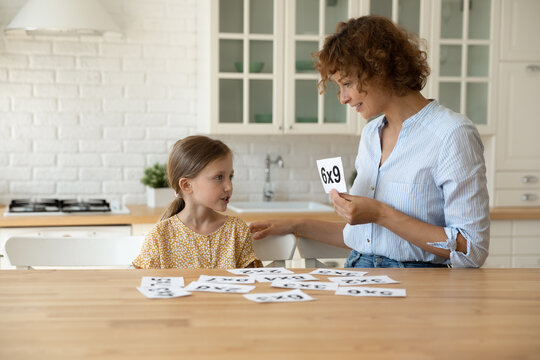 Caring young mother showing paper card with mathematics examples to little 7s kid girl, preparing for examination, enjoying learning or understanding basics in form of game, early development concept.