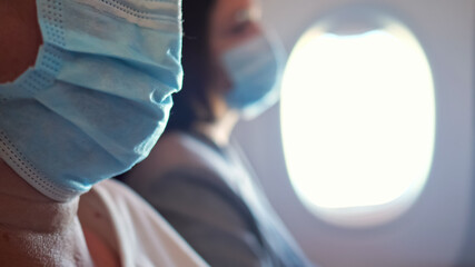 Unrecognizable airplane passengers are flying in medical masks.