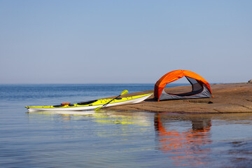 Orange tent, yellow kayak on the island. Kayaking, camping equipment, outdoor activities.