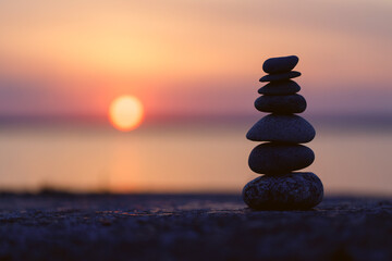 The stones of the pyramid balance on the rock at sunset. The background of the evening sea is blurred. Selective focus.