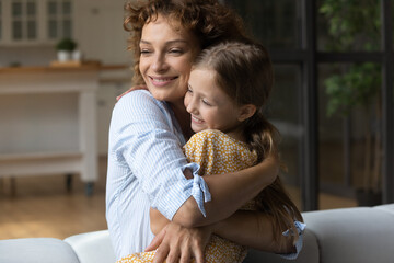 Loving caring 30s young woman embracing cute adopted kid daughter, showing tender feelings indoors....