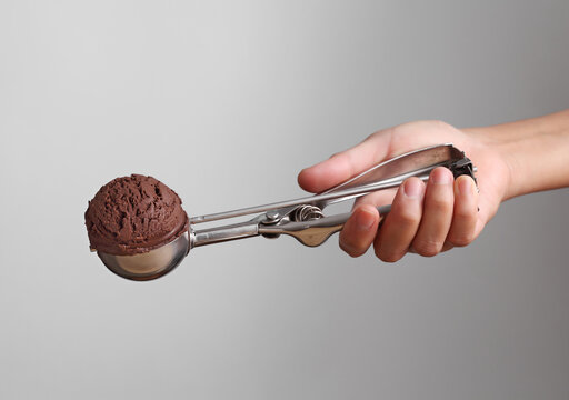 Hand holding chocolate ice cream in spoon for scoop on gray background