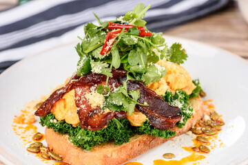 A serving of Chilli Scramble with smoked bacon, shallots, wilted kale and Asian herbs. Served on sourdough bread and shaved parmesan.