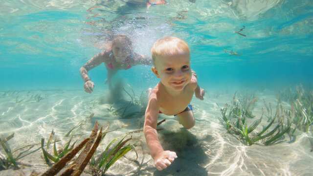 Young mother with child dive in sea lagoon to explore underwater world. Family travel lifestyle in summer adventure camp. Swimming activities on beach vacation with kids.