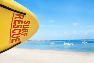 Life saving yellow board with surf rescue sign. Lifeguards stand on duty, look at blue sea....