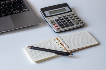 Office desk with spiral notepad, calculator, pen and laptop on white background