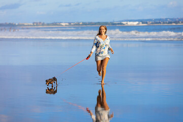 Young happy girl have fun with dachshund dog, run by water pool along sea surf on sand beach....