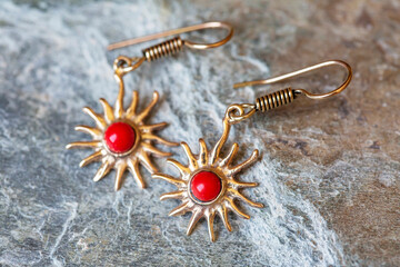 Brass metal pair of earrings on rocky background with mineral stone sea red coral