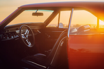 Red retro vintage muscle car interior. Dashboard, steering wheel, seats at sunset