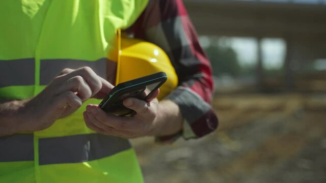Builder In Hard Hat And High Vis Jacket Using Smartphone.