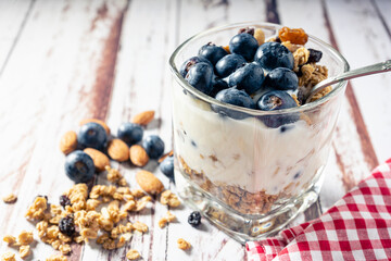 Normal view of a glass with a yogurt, blueberry and granola parfait on a rustic wooden table. Natural eating concept.