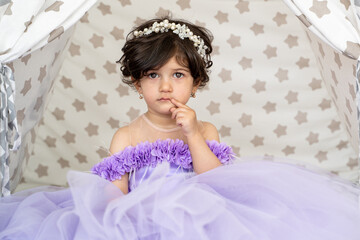 Portait of happy brunette child girl in beautiful purple dress with pearl tiara