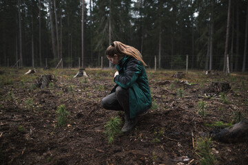 Close up on a young woman middle of the forest preparing to plant a new pine seedling. Young...